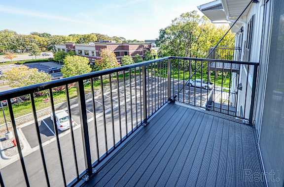 A balcony with a black railing overlooks a parking lot and buildings.