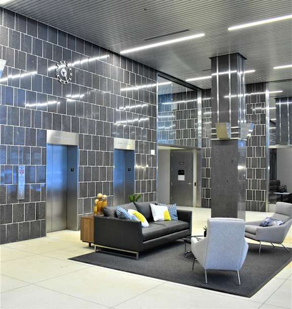 A modern living room with a grey couch, a grey chair and a black and white tiled wall.