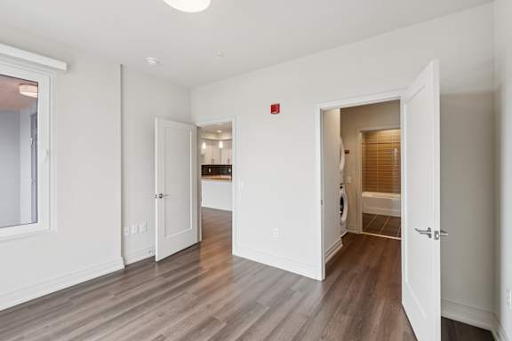 A room with white walls and wooden floors with a doorway leading to another room.