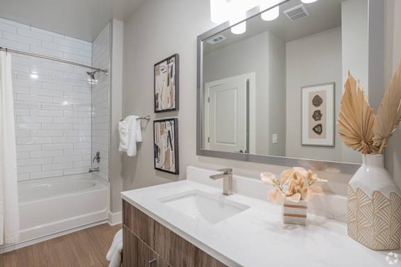 A white sink in a bathroom with a white tub and a mirror.at The Delaney at East Park Apartments, Kennesaw