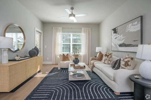 A modern living room with a large rug, a sofa, a coffee table, and a ceiling fan.
