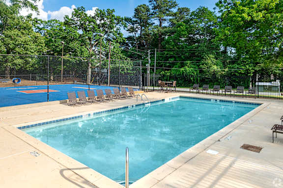 A large outdoor swimming pool surrounded by trees and a fence.