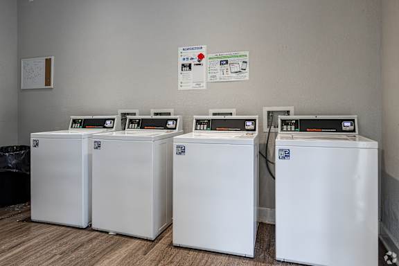Four white washing machines are lined up in a laundry room.