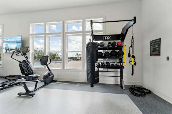 A TRX suspension trainer is hanging from the ceiling in a room with a treadmill, exercise bike, and a punching bag. at The Hendry Apartments, Fort Myers, FL