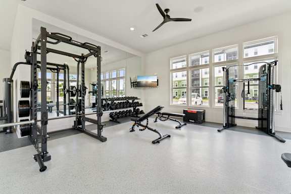 A spacious gym with a variety of equipment including a squat rack, bench, and weights at The Hendry Apartments, Fort Myers, Florida