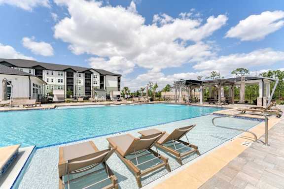 A pool with chairs and a building in the background at The Hendry Apartments, Fort Myers, FL