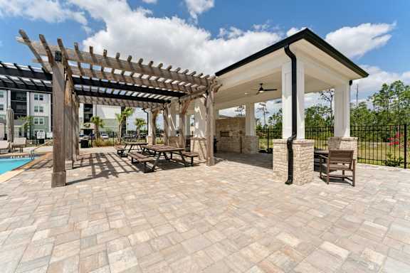 A patio with a pergola and a pool in the background at The Hendry Apartments, Fort Myers, Florida
