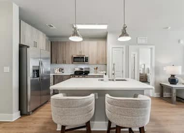 A modern kitchen with a white island and two chairs.