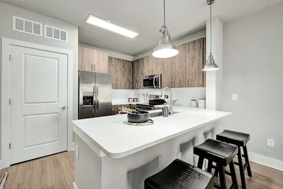 A kitchen with a white countertop and black stools.at The Ashton at East Park Apartments, Kennesaw, Georgia