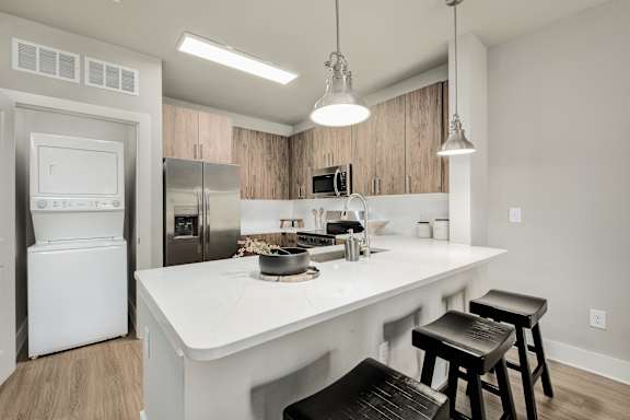 A modern kitchen with a white countertop and black bar stools at The Ashton at East Park Apartments, Georgia