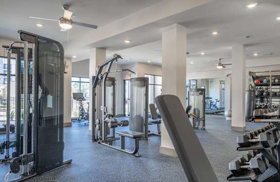 A spacious gym with a variety of equipment including a treadmill, weight bench, and dumbbells at The Delaney at East Park Apartments, Kennesaw