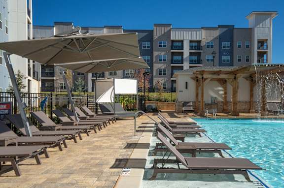 A pool area with sun loungers and a waterfall at The Delaney at East Park Apartments, Georgia, 30144