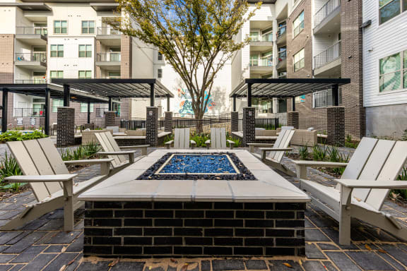 an outdoor patio with a firepit and chairs and an apartment building