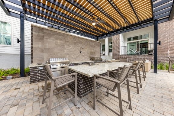 a patio with a long table with chairs and a grill