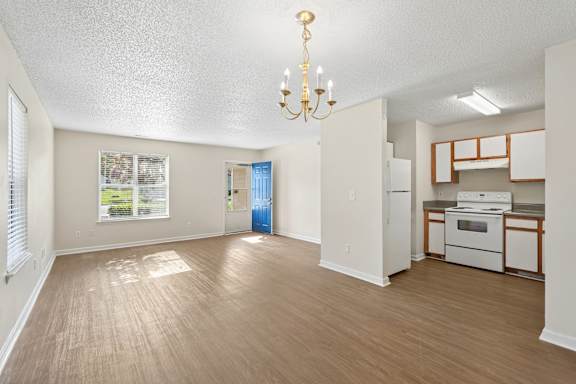 A well-lit, empty room with a chandelier and a kitchenette in the background.