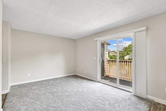 A room with a carpeted floor and a sliding glass door leading to a balcony.