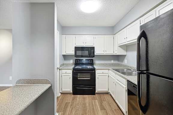 A kitchen with a black refrigerator and white cabinets.