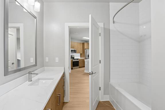 A white bathroom with a sink, mirror, and bathtub.