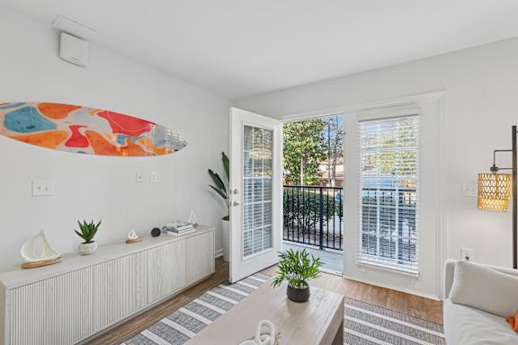 A living room with a white couch, a coffee table, and a surfboard artwork on the wall.