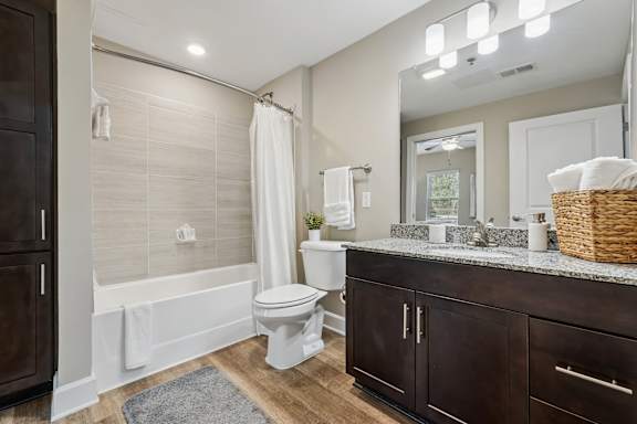 A white toilet sits in a bathroom with a white tub and a white shower curtain.