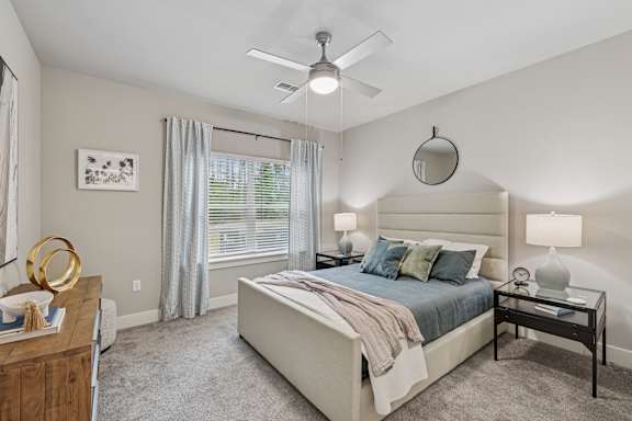 A bedroom with a large bed, a ceiling fan, and a nightstand with a lamp.