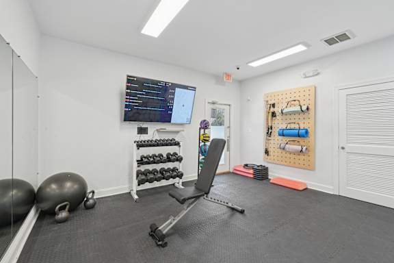 A gym room with a bench, weights, and a screen.