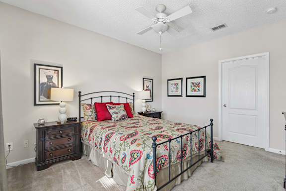 A bedroom with a bed, dresser, and ceiling fan.