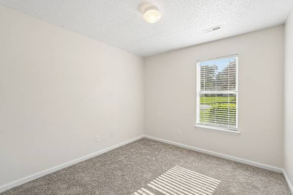 A room with a carpeted floor and a window with blinds.