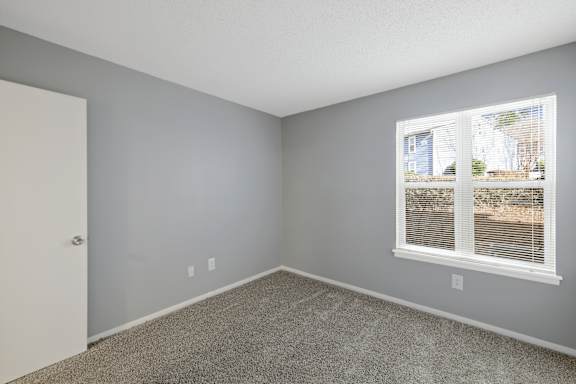 A room with a carpeted floor, a window with blinds, and a door.