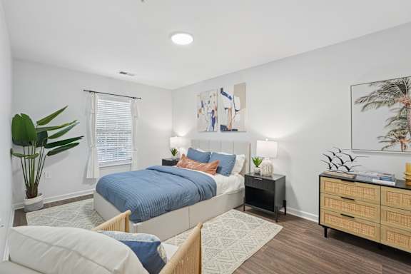 A bedroom with a bed, nightstand, and a plant.