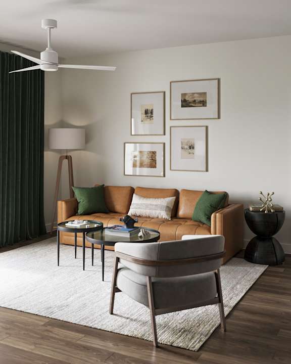 A living room with a brown leather couch, a grey armchair, a coffee table, and a ceiling fan at The SoHo Luxury Apartments, Raleigh, NC