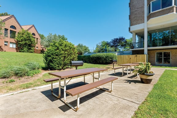 two picnic tables outside of an apartment building with a grill