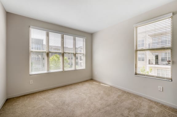 an empty bedroom with three windows and a carpeted floor