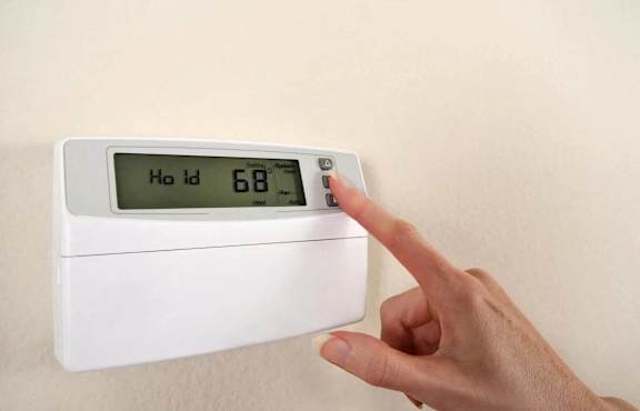 A person is pointing at a thermostat that reads 68.