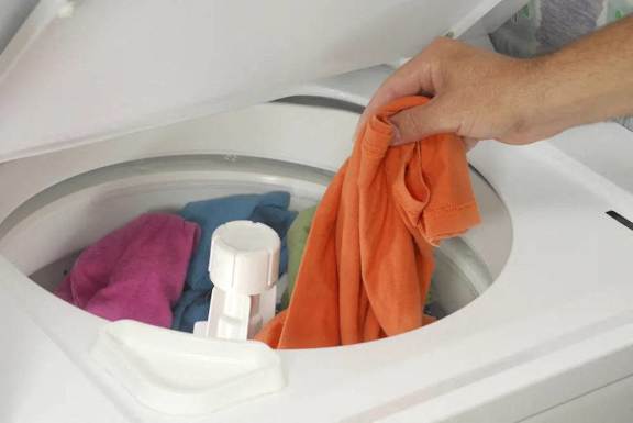A person is putting a orange towel into a washing machine.