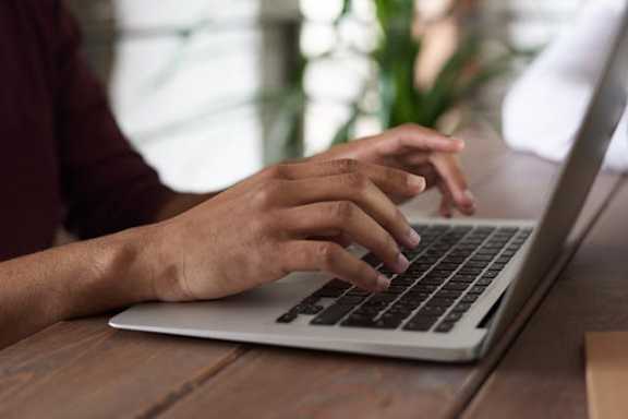 A person's hands are typing on a laptop keyboard.