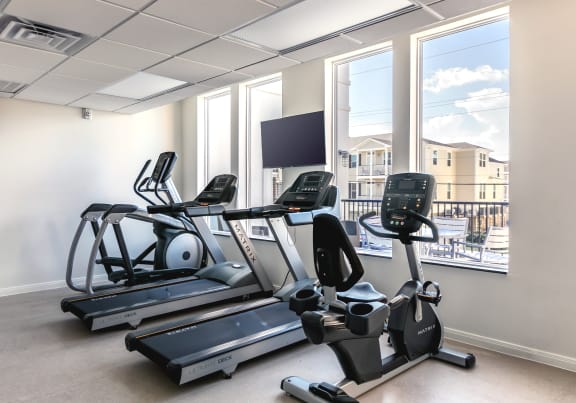 two treadmills and a tv in a room with windows at Cedars at Carver Park Apartments