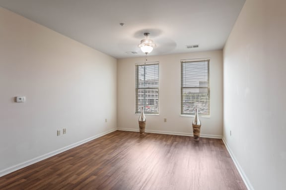 an empty living room with wood flooring and two windows