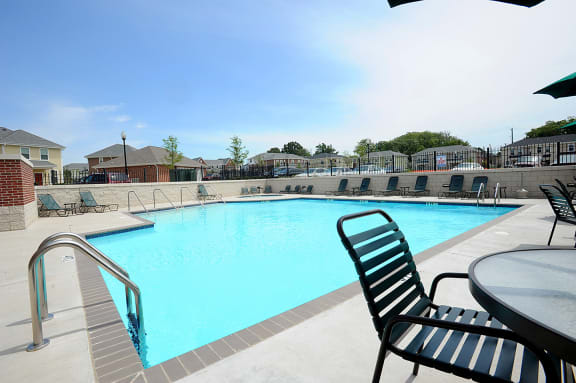 our resort style swimming pool is next to our apartments with chairs and a table