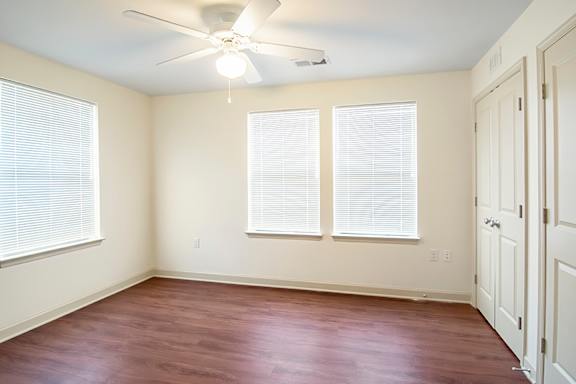 A room with a ceiling fan and three windows.