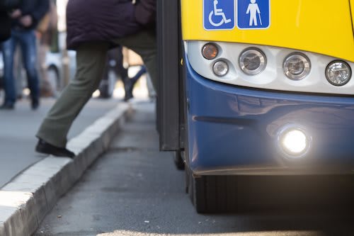 A person in a purple coat is walking past a bus with a handicap sign on the front.