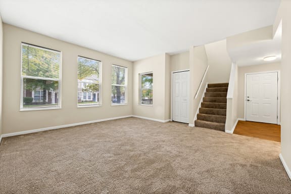 an empty living room with a staircase and three windows