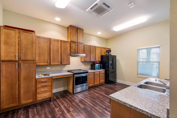 a kitchen with wood cabinets, black and stainless appliances and granite counters at Wheatley Senior Living San Antonio