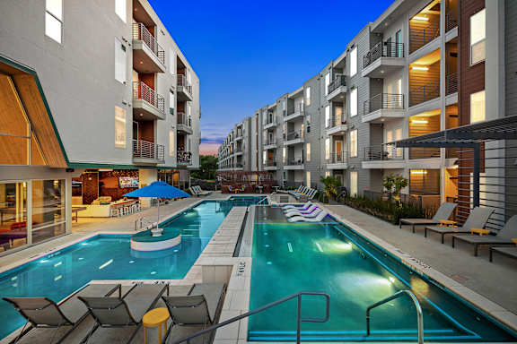 A swimming pool in a residential area with lounge chairs and umbrellas.