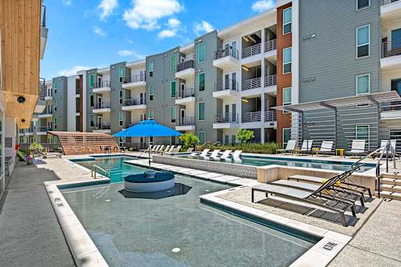 A swimming pool with a slide and sun loungers in front of apartment buildings.