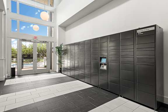 A large, black, metal storage unit with a digital display and keypad is situated in a room with a tiled floor and a glass door with a red exit sign above it.