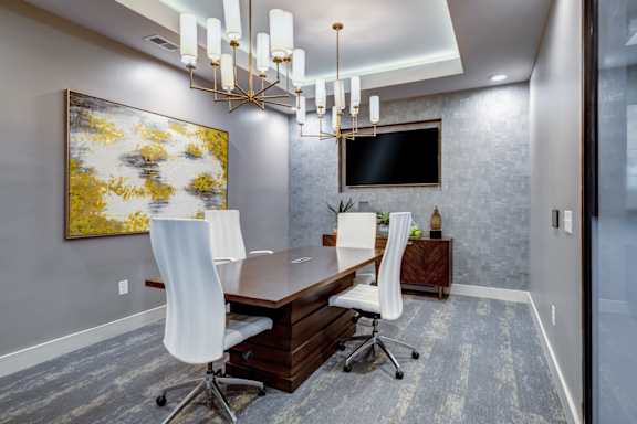 A modern conference room with a large painting on the wall and a TV above the desk.