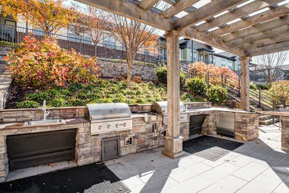 A stone patio with a grill and a pergola.