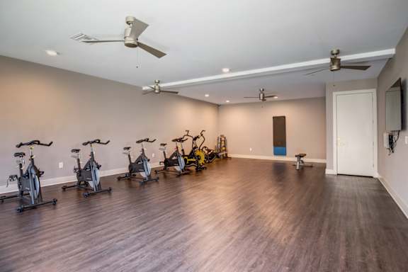 A room with a wooden floor and a wall of exercise bikes.