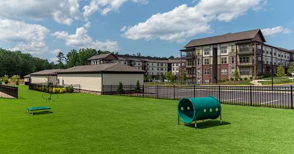 A green plastic barrel sits on a green lawn in front of a large building.